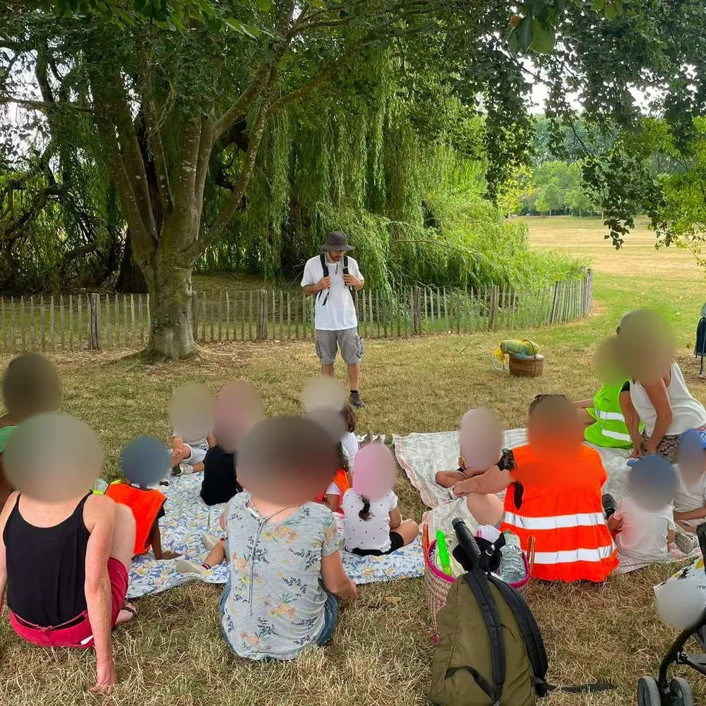 Fabrice avec des enfants et leurs accompagnants sous les arbres, visages des participants floutés